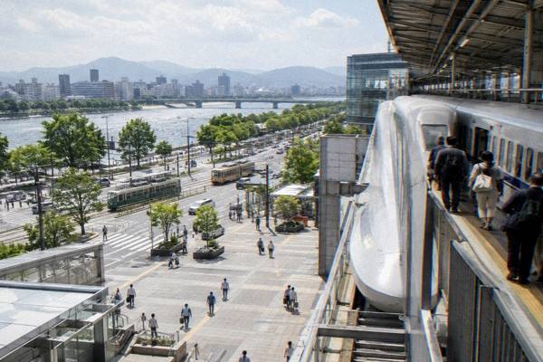 A sleek bullet train stops at Hiroshima Station as travelers step off with backpacks.