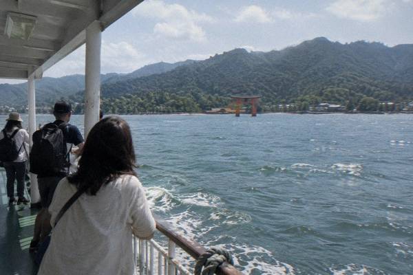 A ferry crosses the water toward Miyajima with the great torii gate rising ahead.
