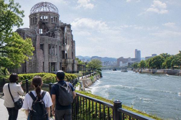 A licensed guide leads a small group of visitors along the riverside promenade in central Hiroshima.