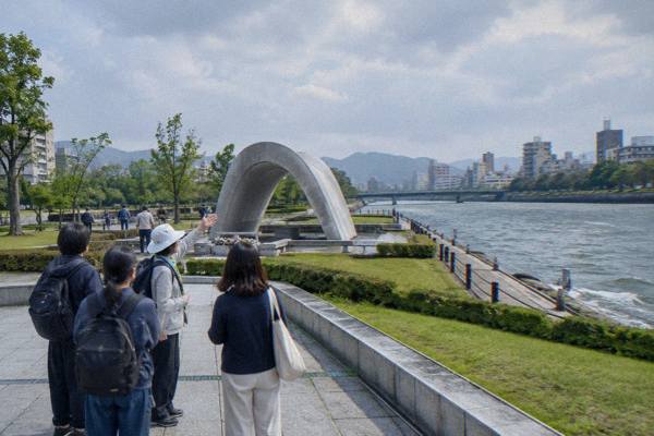A guide speaks to a small group of visitors on a riverside path near the Atomic Bomb Dome.