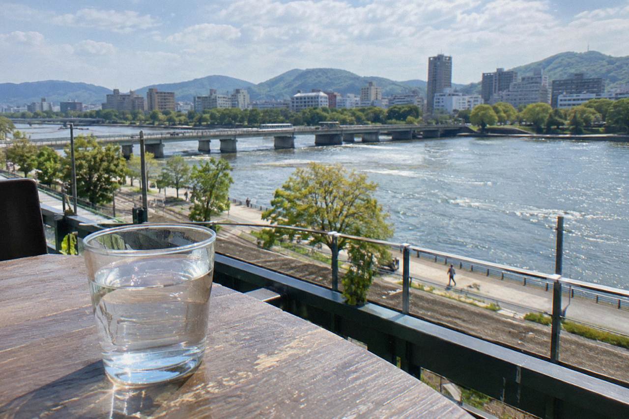 A glass of clear tap water on a table with the Hiroshima city skyline in the background