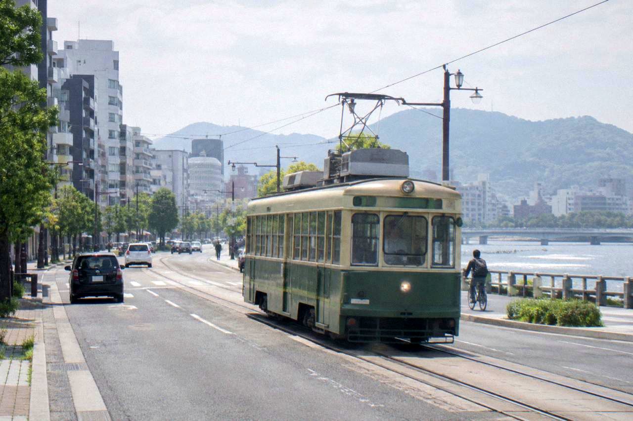 A Hiroden streetcar travelling along a city street in Hiroshima with buildings on both sides