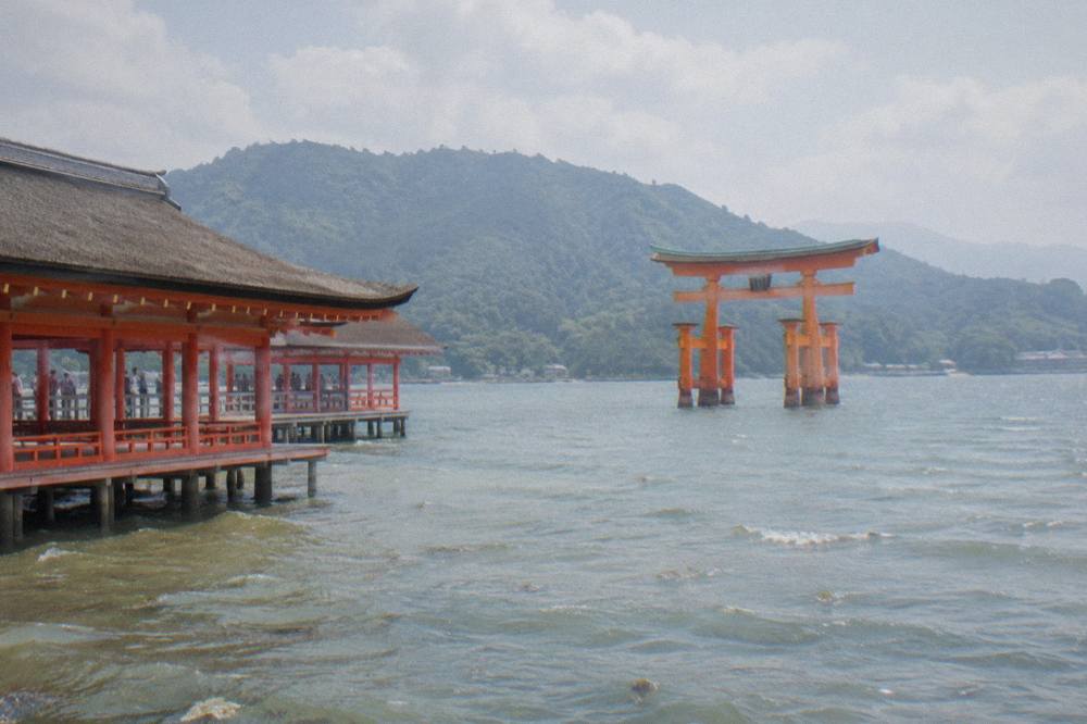The Great Torii of Itsukushima Shrine standing in the shallow water at Miyajima with the wooded island behind it