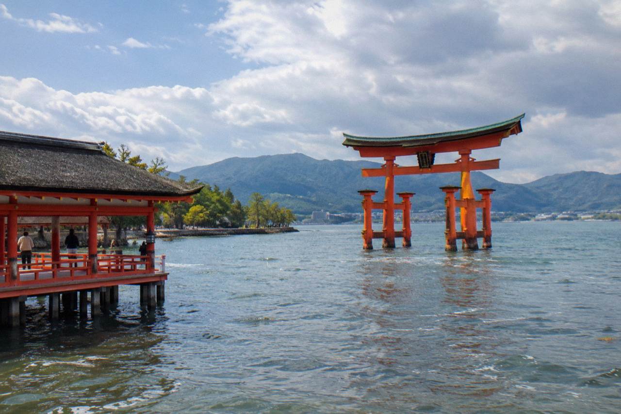 The red Great Torii of Itsukushima Shrine standing in shallow water at Miyajima with wooded hills behind