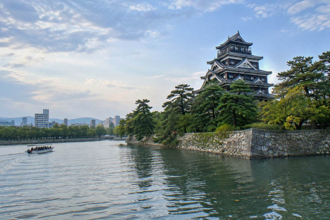 The white keep of Hiroshima Castle rising above its moat and stone walls, seen from the castle grounds