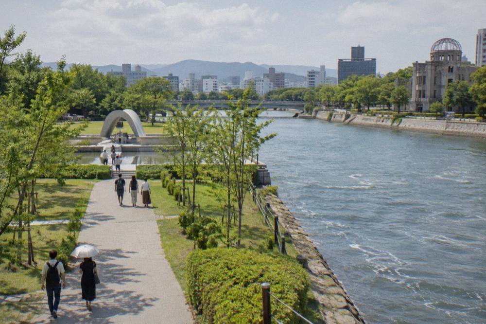 Visitors walking quietly along a tree-lined path in Hiroshima Peace Memorial Park toward a memorial monument