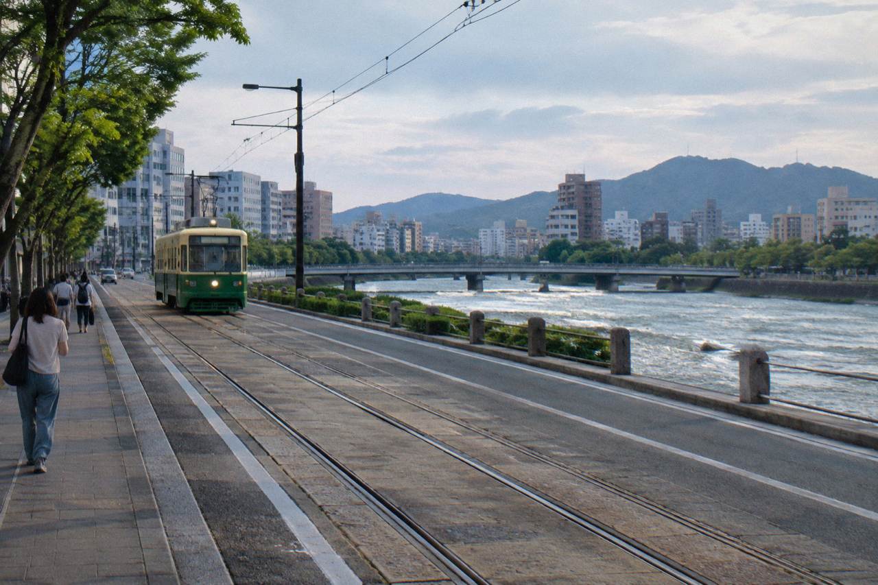 A wide Hiroshima city street with streetcar tracks running down the middle and pedestrians on the sidewalk