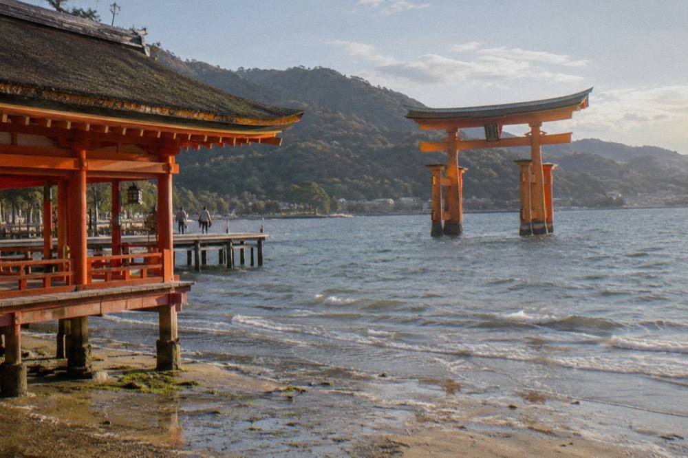 The Great Torii of Itsukushima Shrine standing in the shallows at Miyajima with wooded hills behind