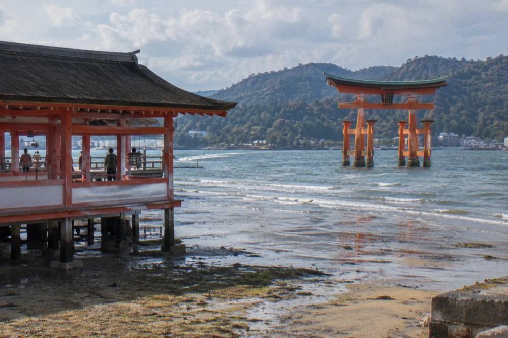 The Great Torii of Itsukushima Shrine on Miyajima standing in shallow water at low tide with the wooded island behind