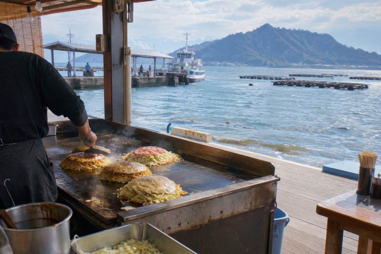 A Hiroshima style okonomiyaki being cooked in layers on a hot iron griddle
