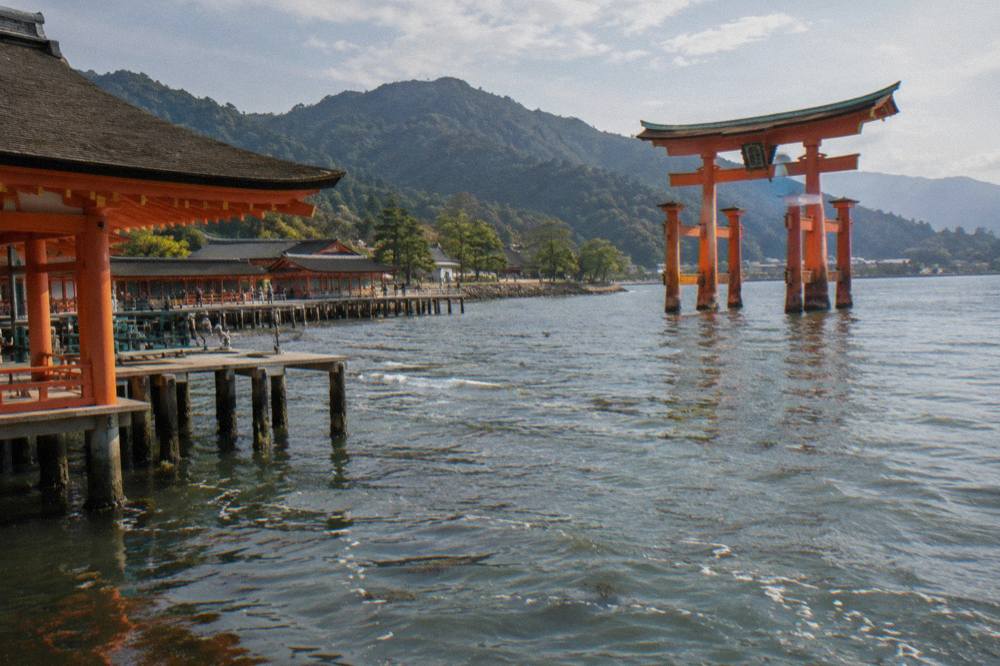 The red Great Torii of Itsukushima Shrine standing in shallow water at Miyajima with the shrine buildings behind