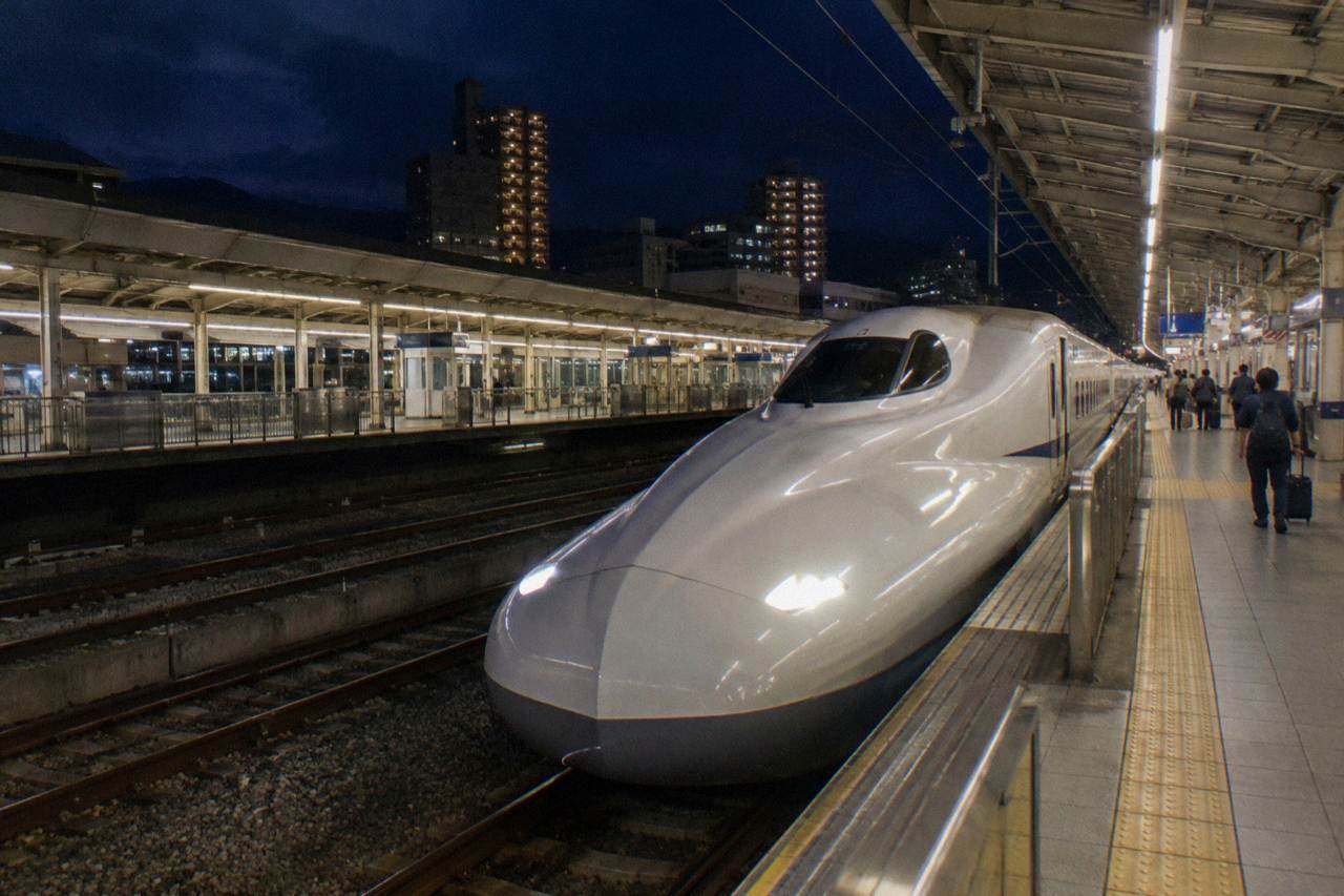 A sleek bullet train platform at Hiroshima Station at night with the train waiting under bright lights
