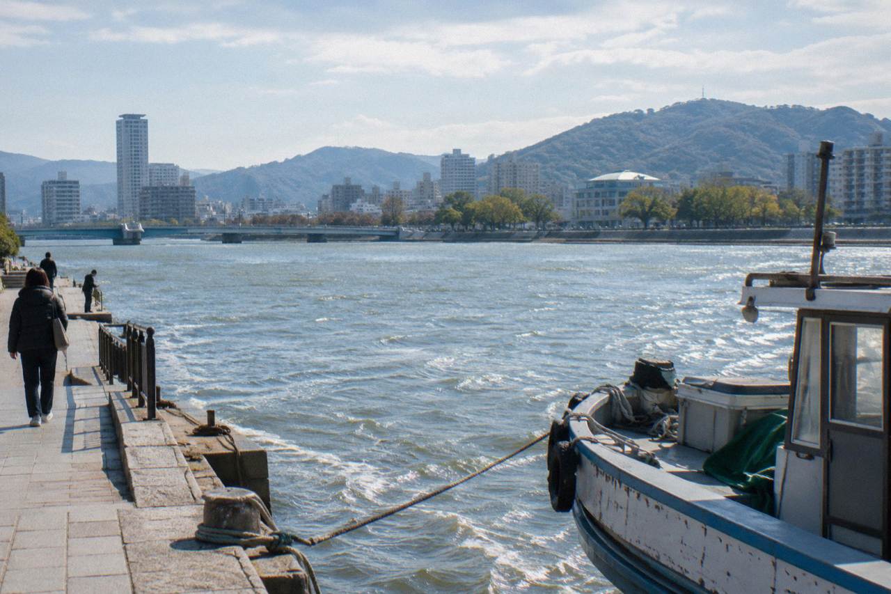 City buildings rising from a river delta with forested hills and a broad bay behind them