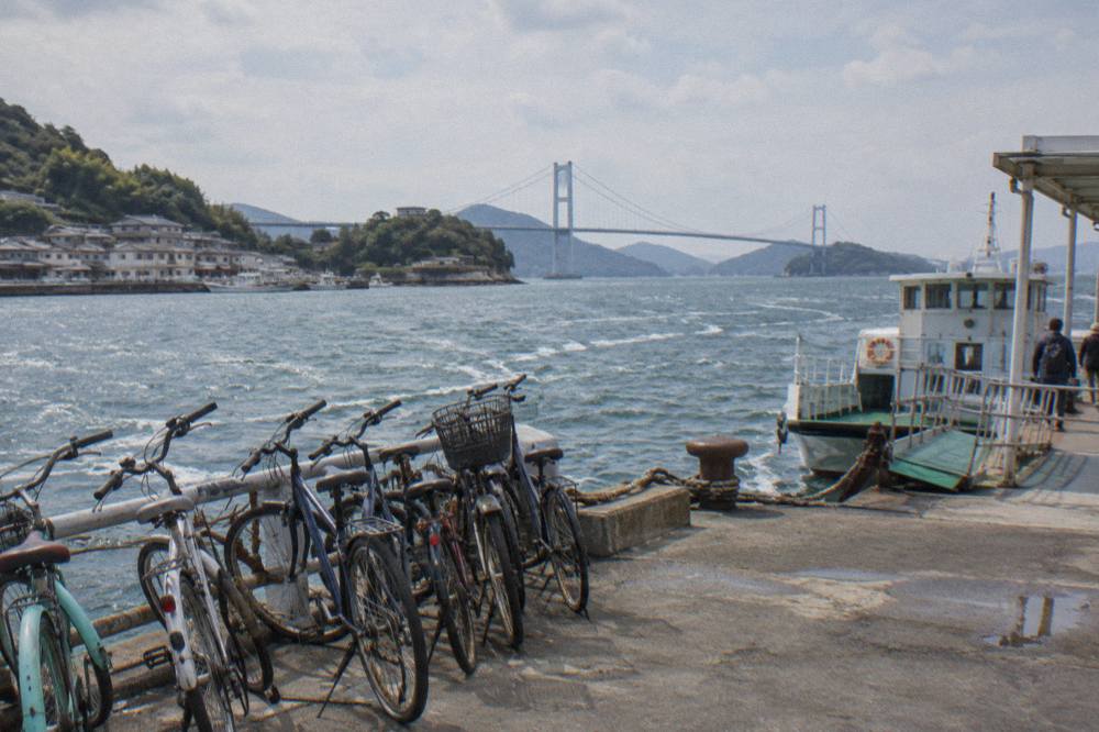 A small island town with a harbour and low buildings seen from a coastal road