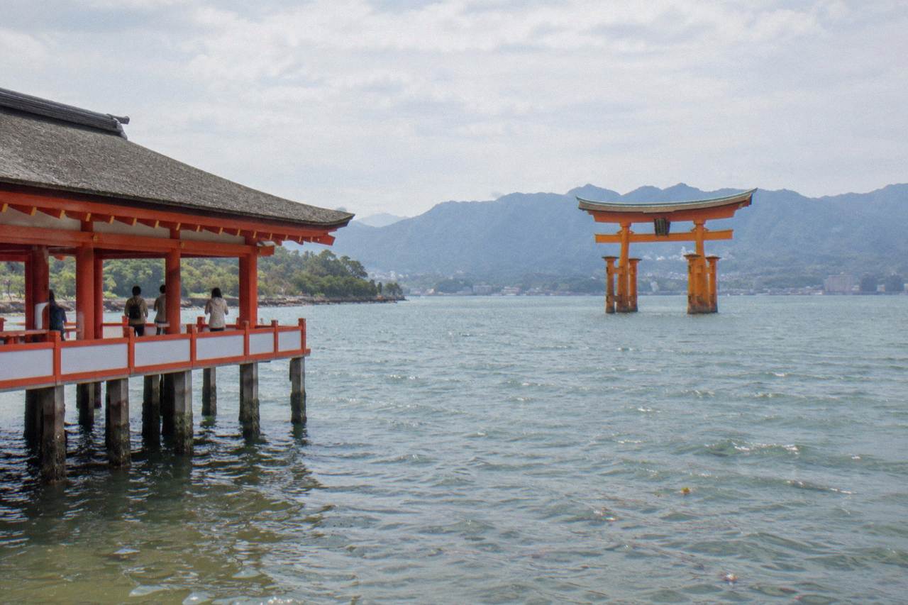 The Great Torii of Itsukushima Shrine standing in the water at Miyajima with forested hills behind