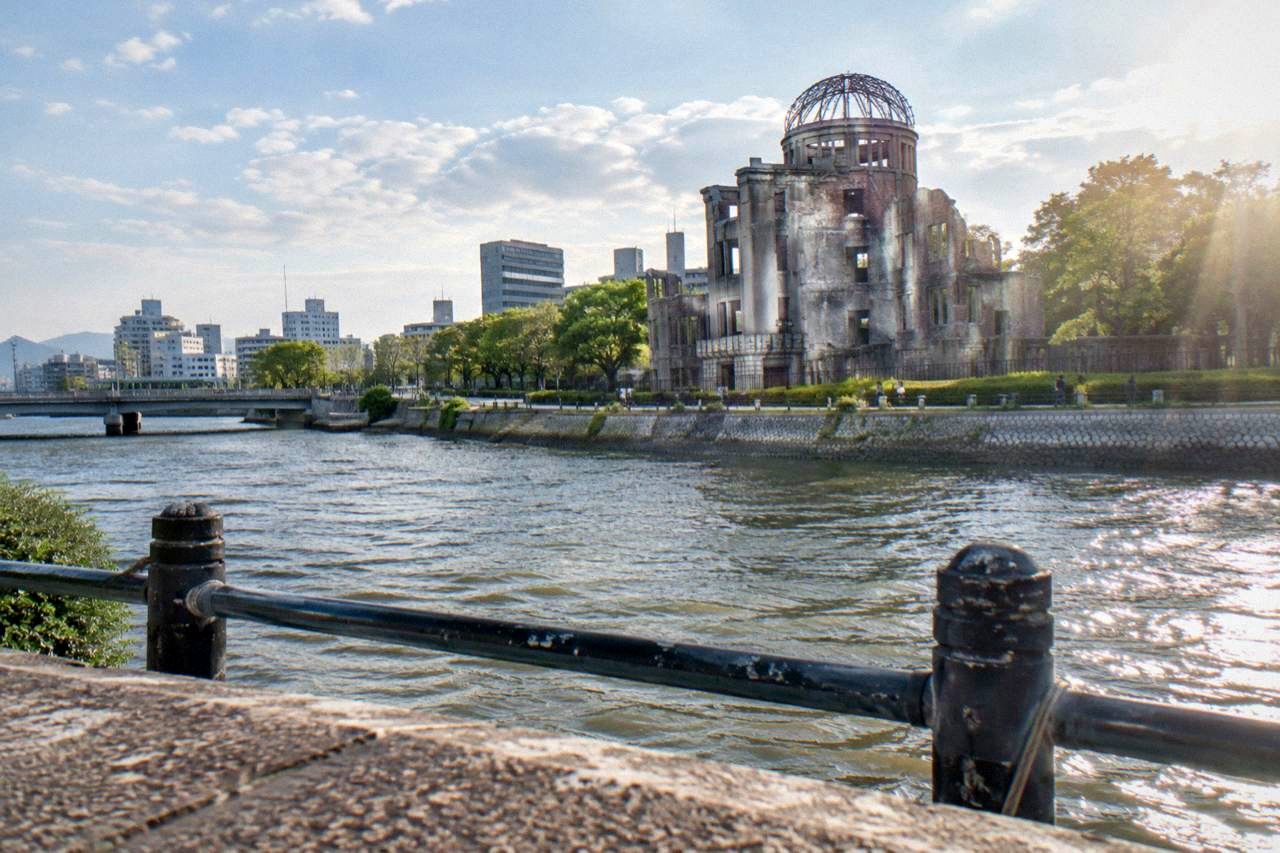 The Peace Memorial Park in Hiroshima with green lawns, the A-Bomb Dome across the river, and modern buildings behind it