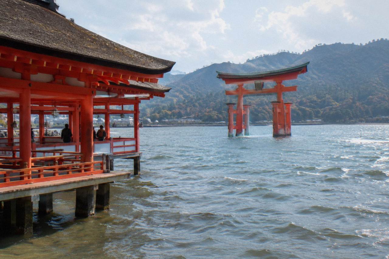 The red Great Torii of Itsukushima Shrine standing in shallow water on Miyajima with wooded hills behind