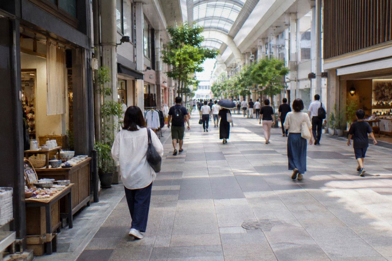 A covered shopping arcade in central Hiroshima with pedestrians walking past small storefronts