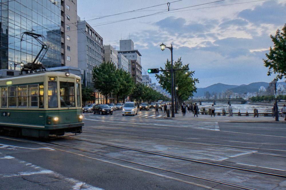 A busy downtown intersection in Hiroshima with streetcar tracks crossing in front of department stores