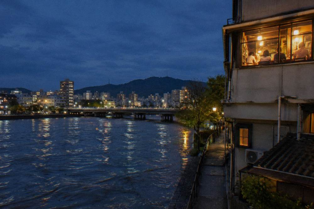 A small izakaya counter restaurant glowing on an upper floor of a downtown Hiroshima building at night