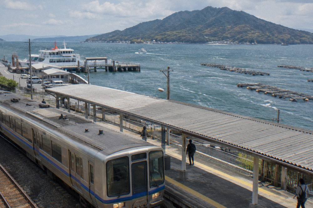 JR train arriving at Miyajimaguchi Station platform with ferry terminal beyond