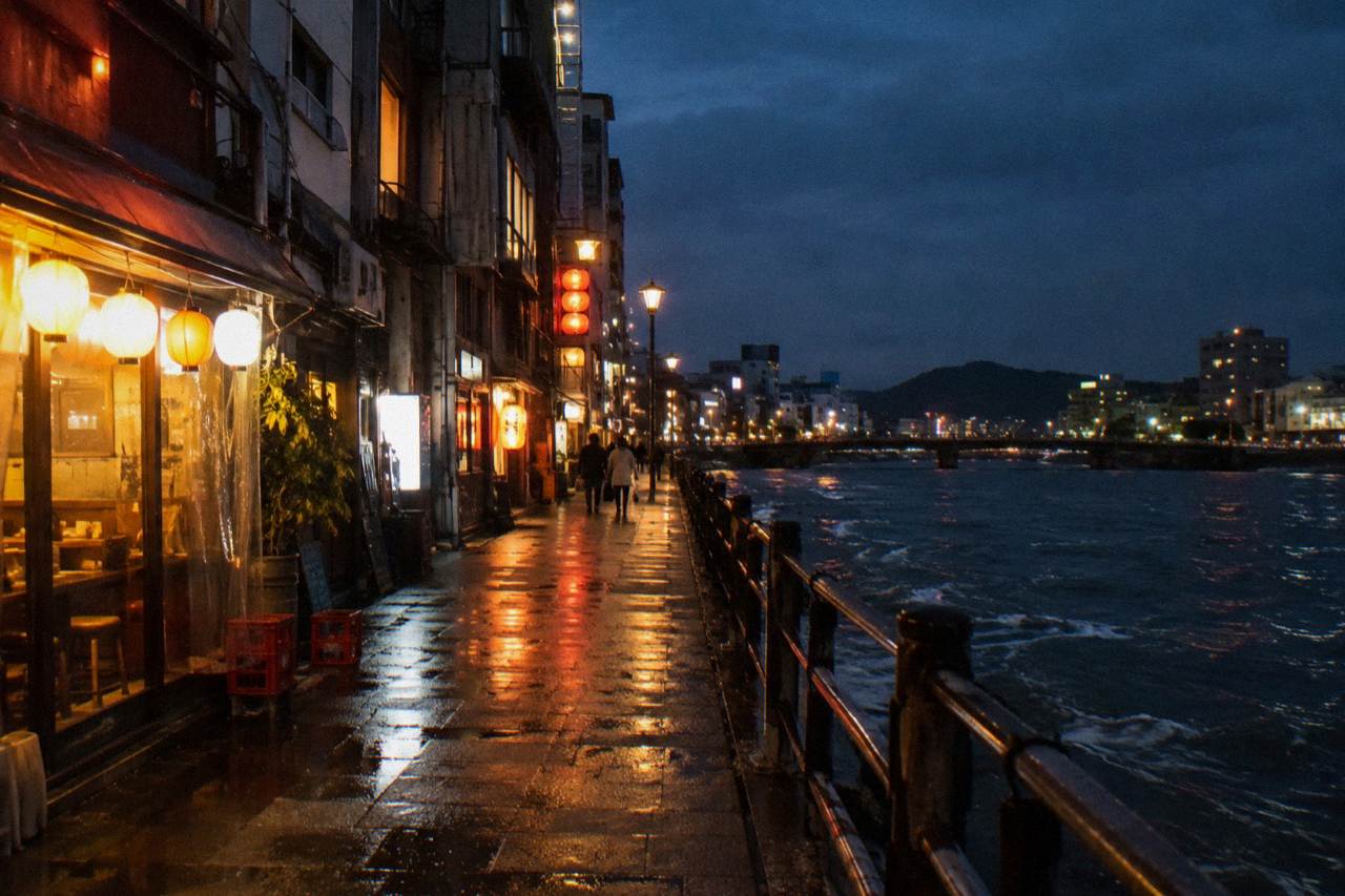 A narrow illuminated bar street in Nagarekawa, Hiroshima, at night with neon and izakaya fronts