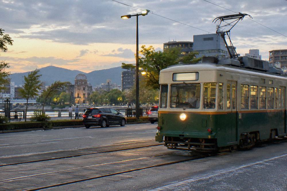 A Hiroden streetcar moving through a lit downtown Hiroshima street in the evening