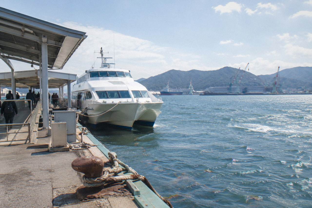Ferry docked at a passenger terminal in Hiroshima with calm harbor water and hills beyond