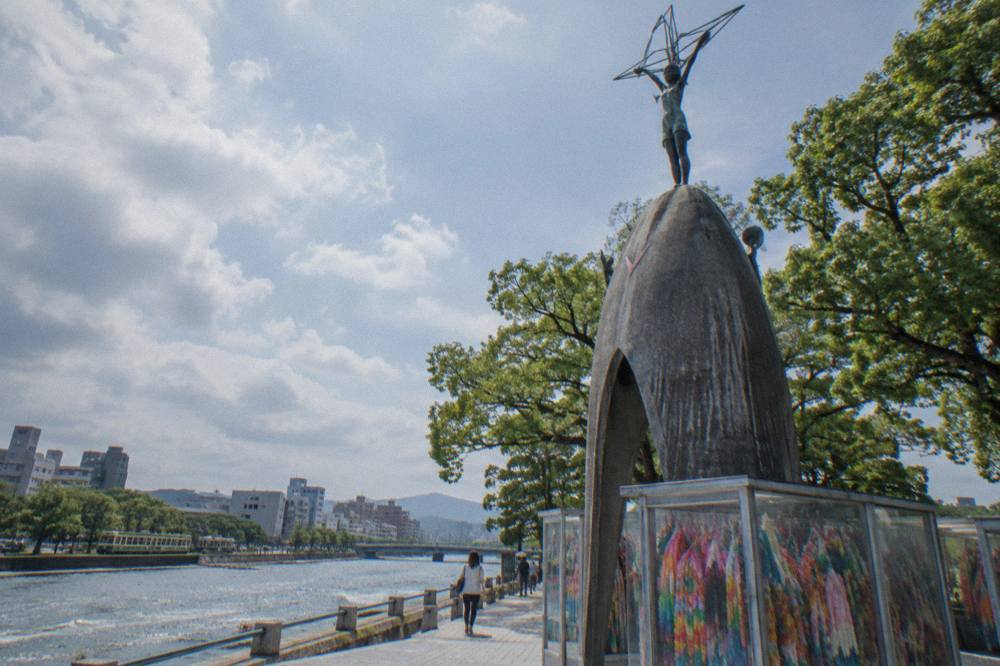 Bronze figure reaching upward atop a dark stone mound surrounded by glass cases of colorful folded paper cranes
