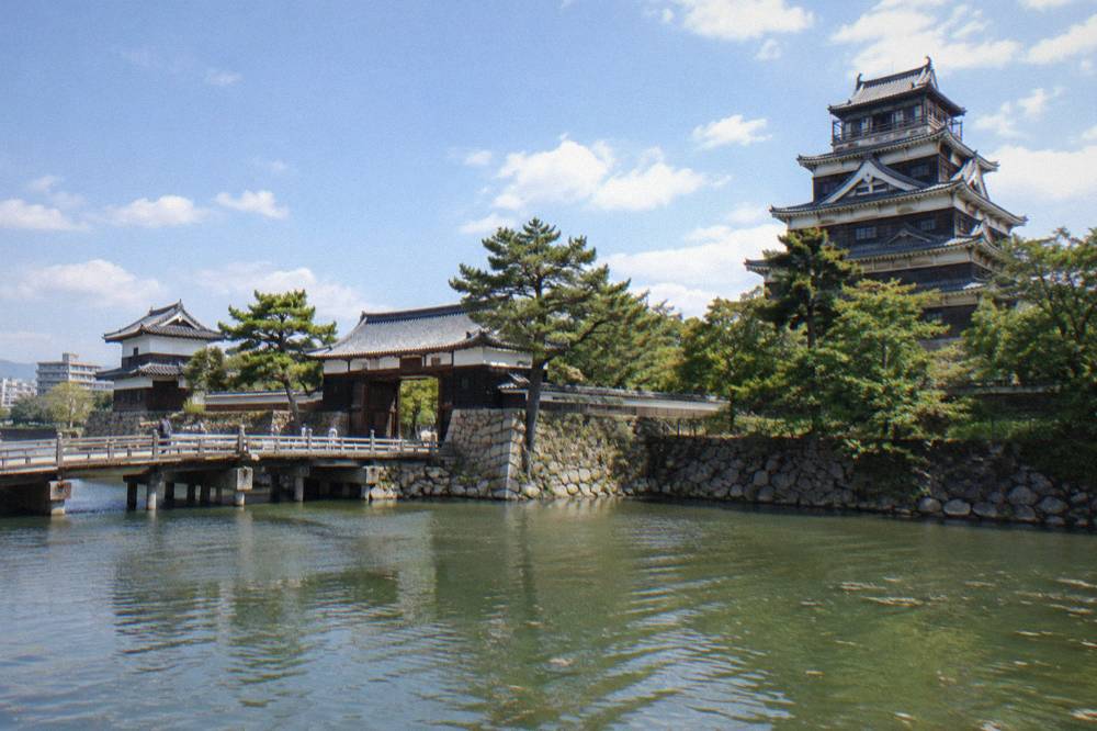 A reconstructed timber castle gate and turrets seen across a moat, with a stone bridge leading to the entrance.