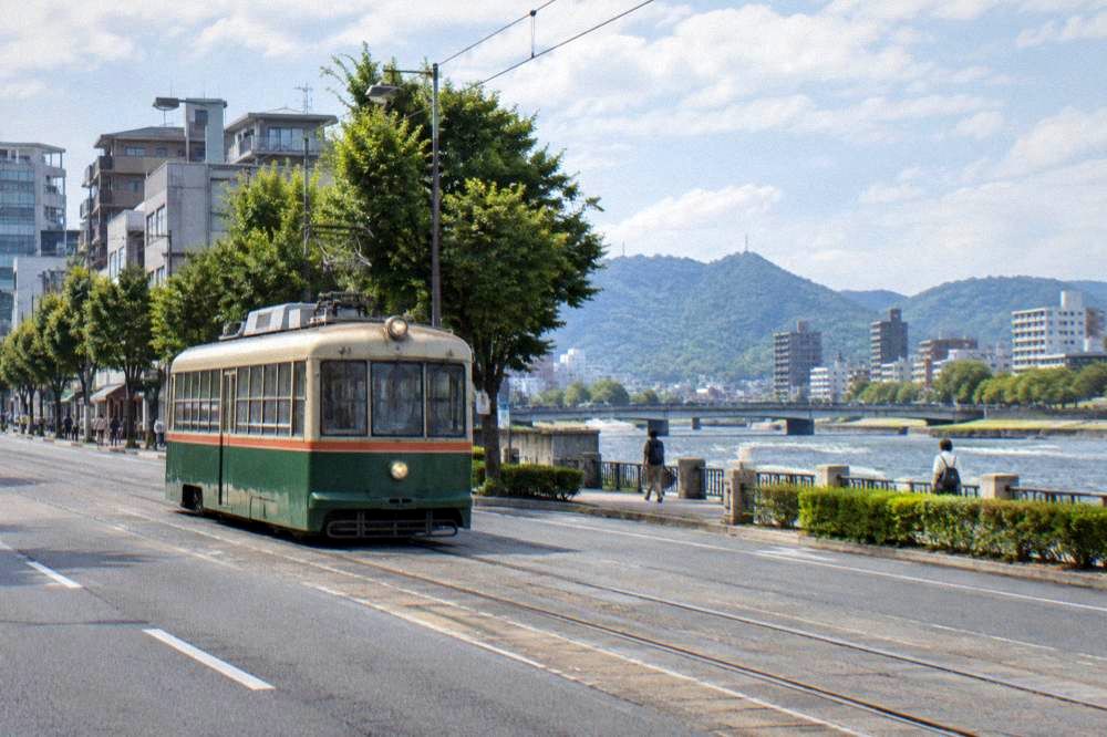 A Hiroden tram in central Hiroshima seen from street level, with shops along the road.