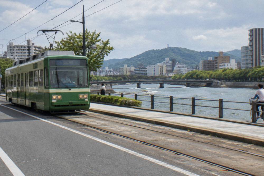 A green Hiroden tram moving along a city street in Hiroshima
