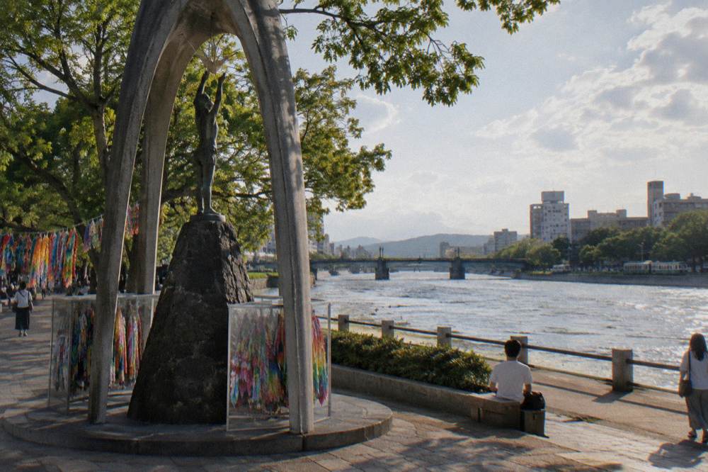 Stone monument sheltered under a bell-shaped canopy with colourful folded paper crane garlands strung nearby