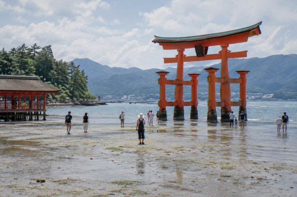 Visitors standing on the exposed seabed beside the base of the Great Torii at low tide