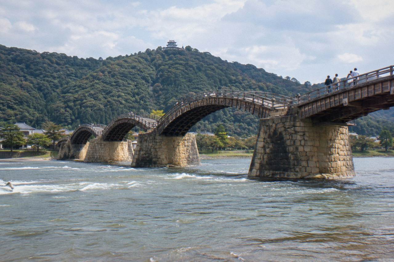 Five wooden arches of the Kintaikyo Bridge crossing the Nishiki River with forested hills behind