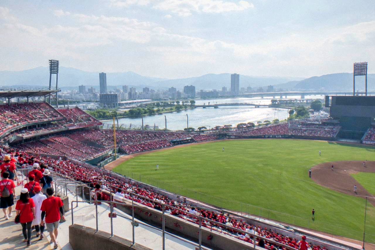 A modern baseball stadium under a bright sky with green field and stands of spectators