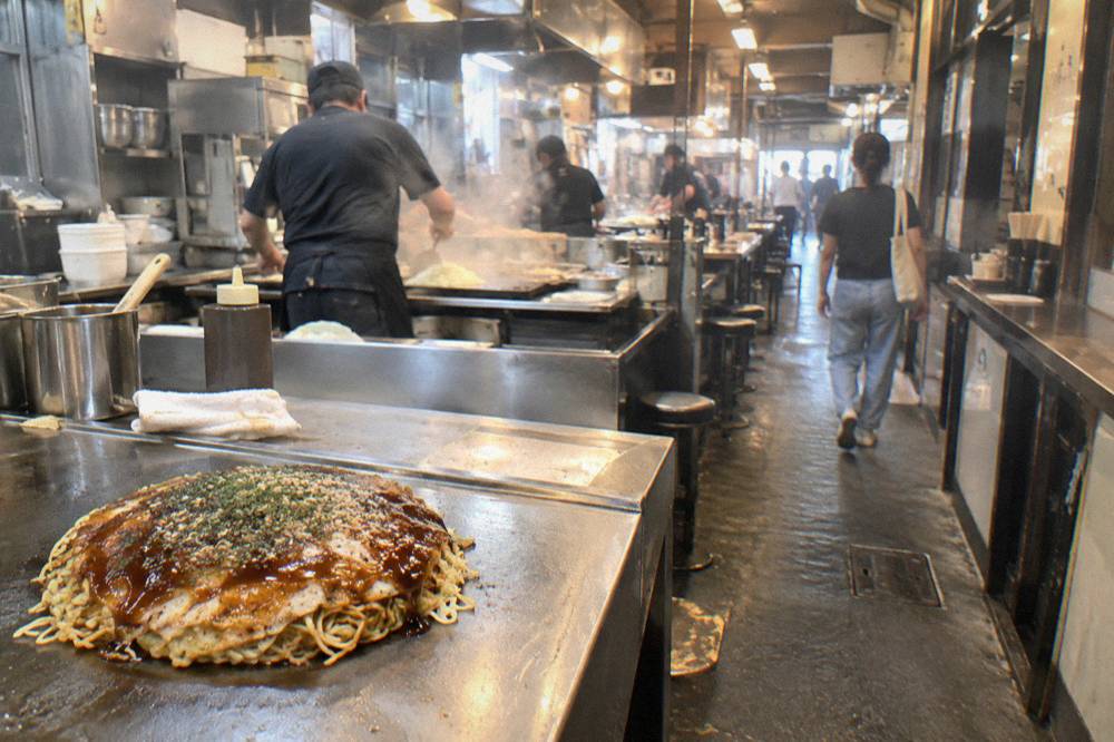 A freshly finished Hiroshima okonomiyaki with noodles, cabbage and sauce on a steel plate