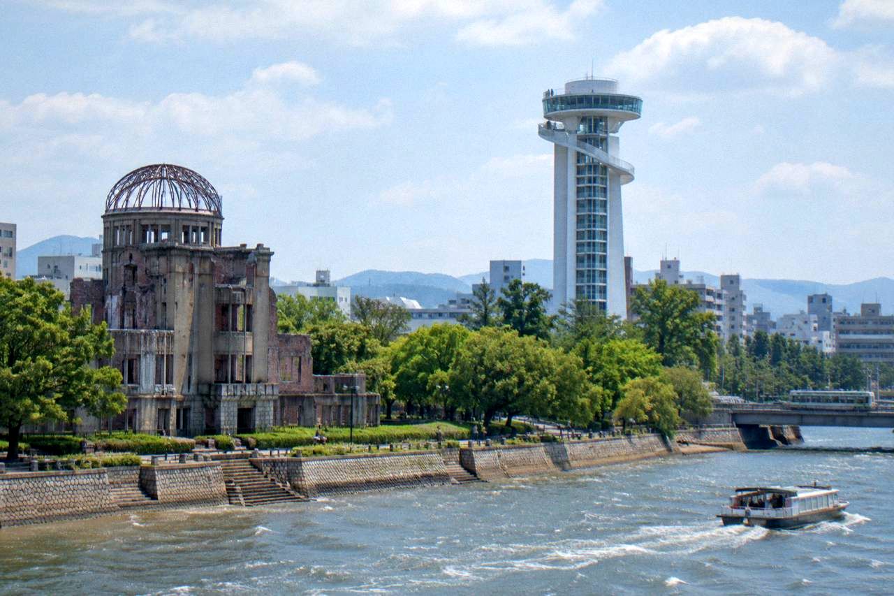 A modern observation tower rising above trees beside a river, with a preserved ruin in the foreground