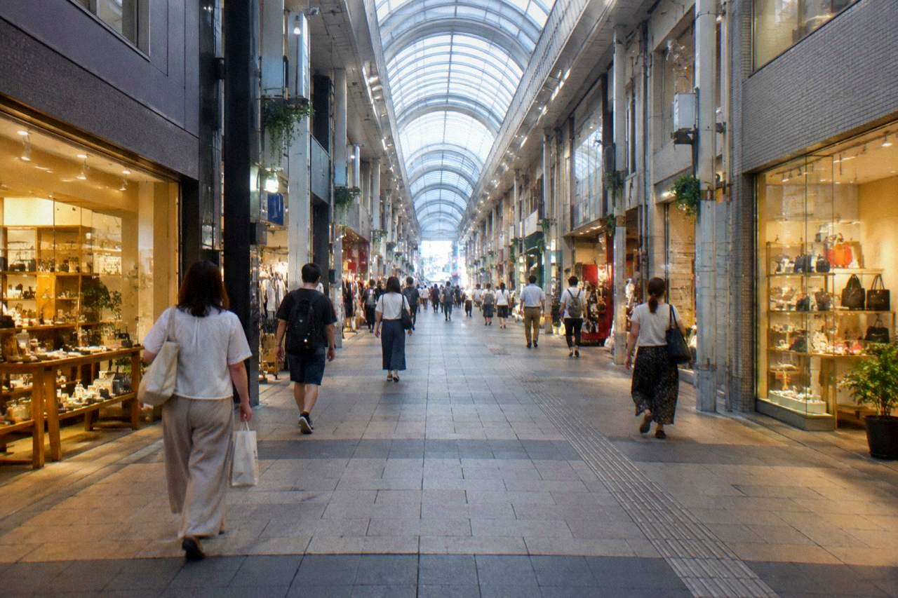 A covered pedestrian shopping arcade in Hiroshima with illuminated shop fronts and people walking in the evening