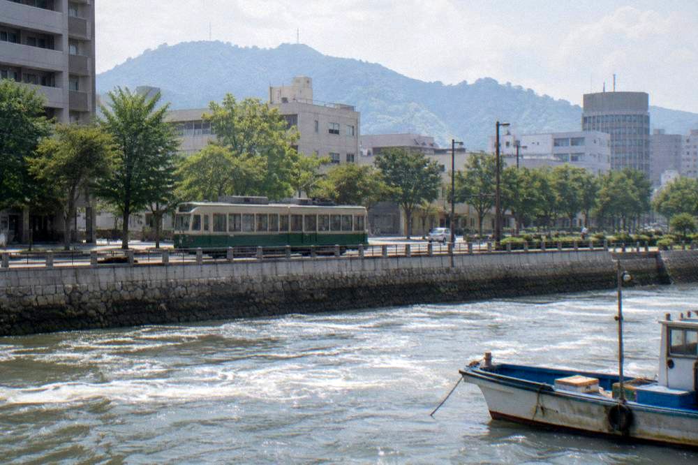 A green Hiroden streetcar moving along a downtown Hiroshima street