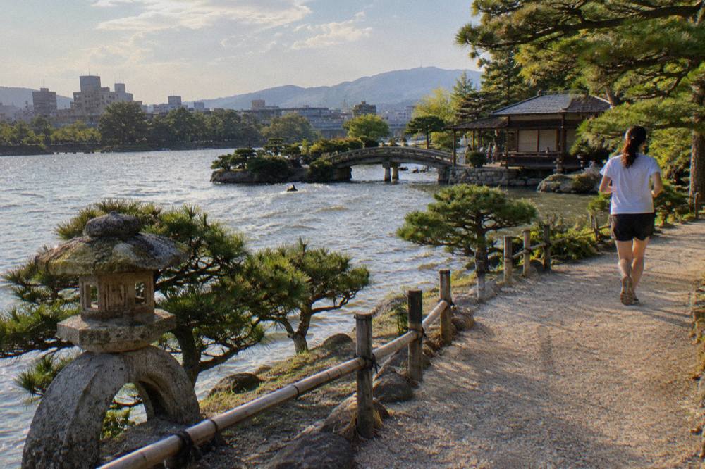 A gravel path curving beside a pond between clipped pines and stone lanterns in a Japanese garden