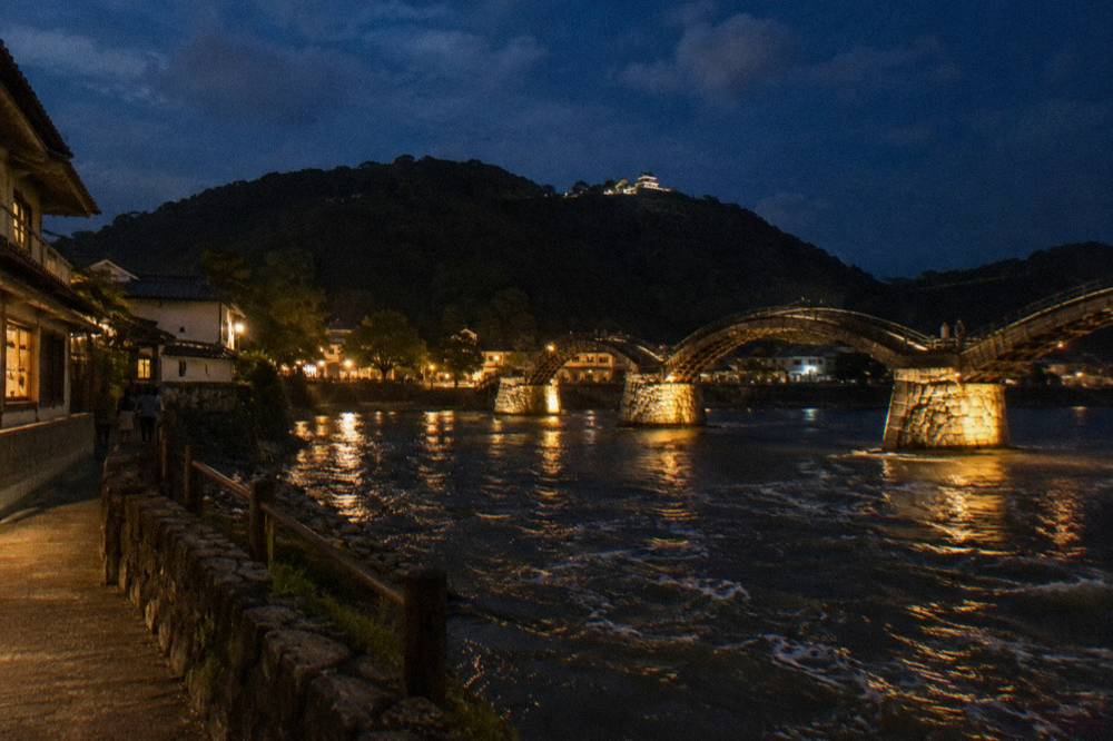 Nighttime illumination lighting the arches of a wooden bridge over dark river water