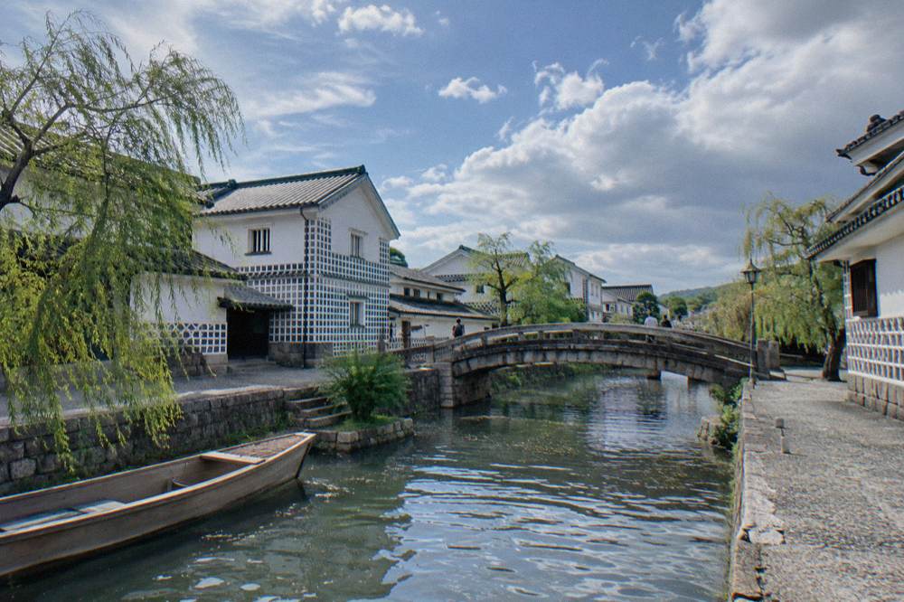 Stone bridge crossing a narrow canal between white walled merchant houses in Kurashiki