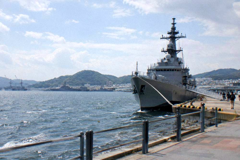 A large grey naval ship moored at a quay in Kure with a gangway ashore
