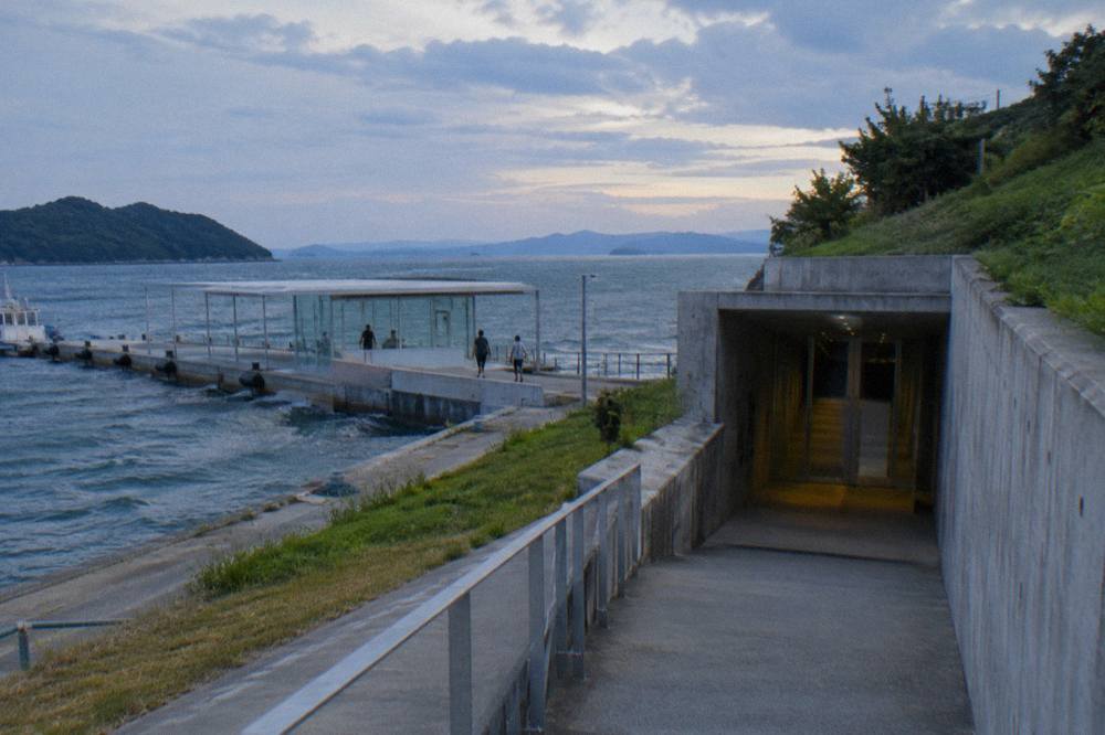 A concrete museum entrance built into a hillside with a view of calm sea beyond