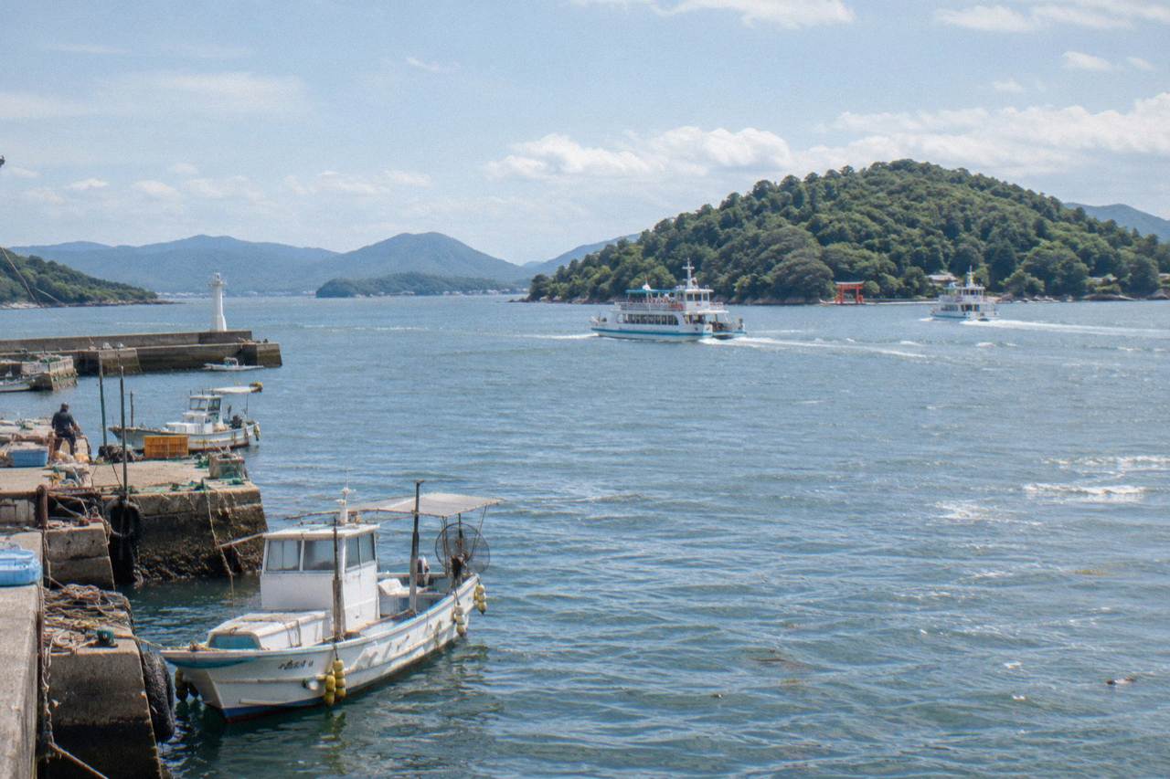 Ferry boats crossing calm water toward a wooded island with a red gate on the shoreline