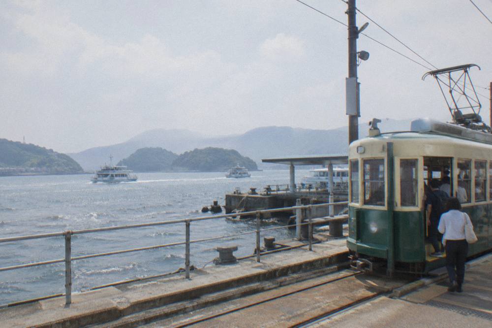 A streetcar at a waterside stop with passengers boarding near a ferry terminal