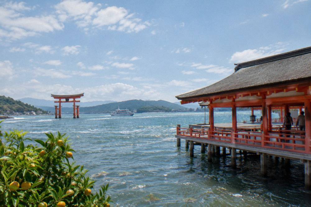 A vermilion shrine corridor standing over seawater with a large wooden gate offshore