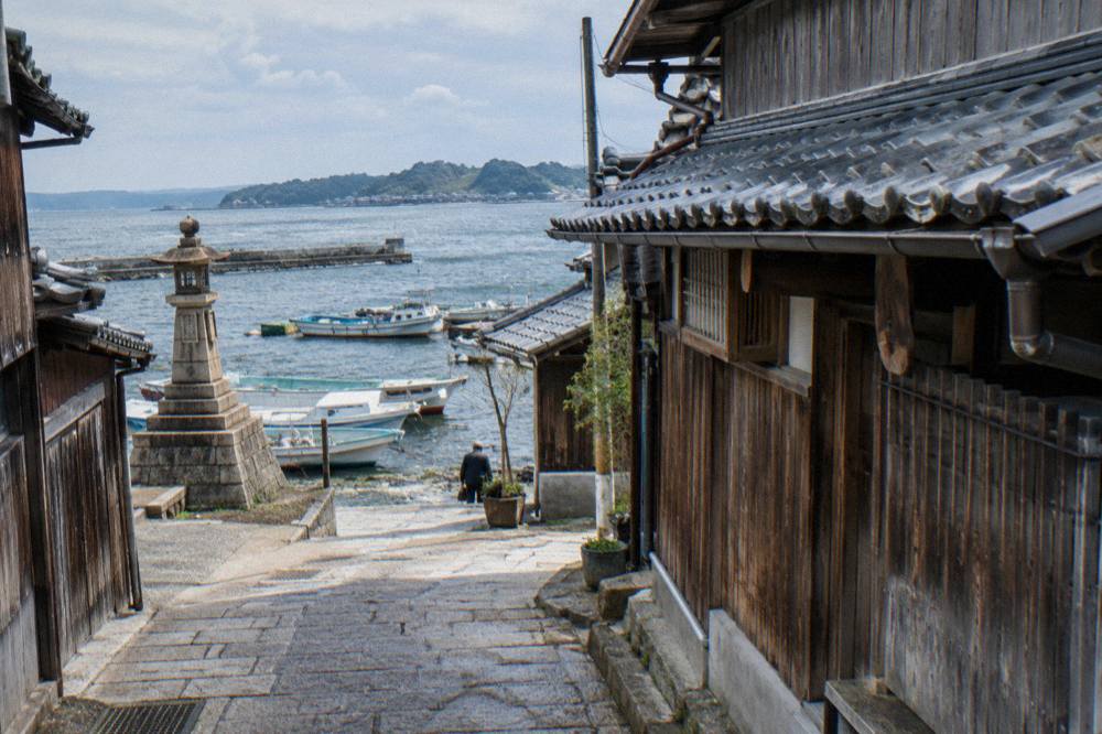 Narrow stone-paved alley between old wooden merchant houses with tiled roofs in a Japanese port town