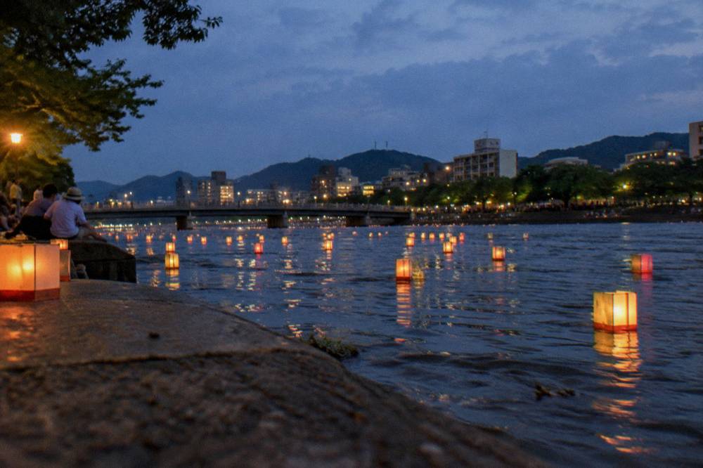 Paper lanterns floating on a river in Hiroshima at dusk during the August memorial period